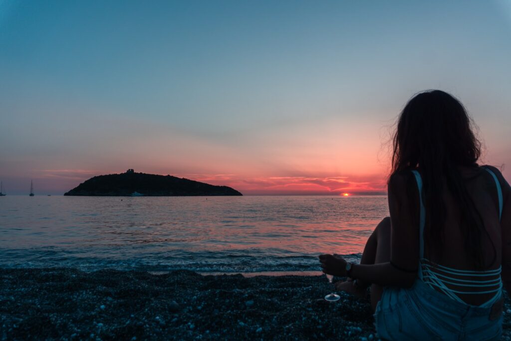 海辺で寂しそうに夕日を見る女性